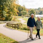 A happy senior couple holding hands and walking on a paved pathway in a park during autumn
